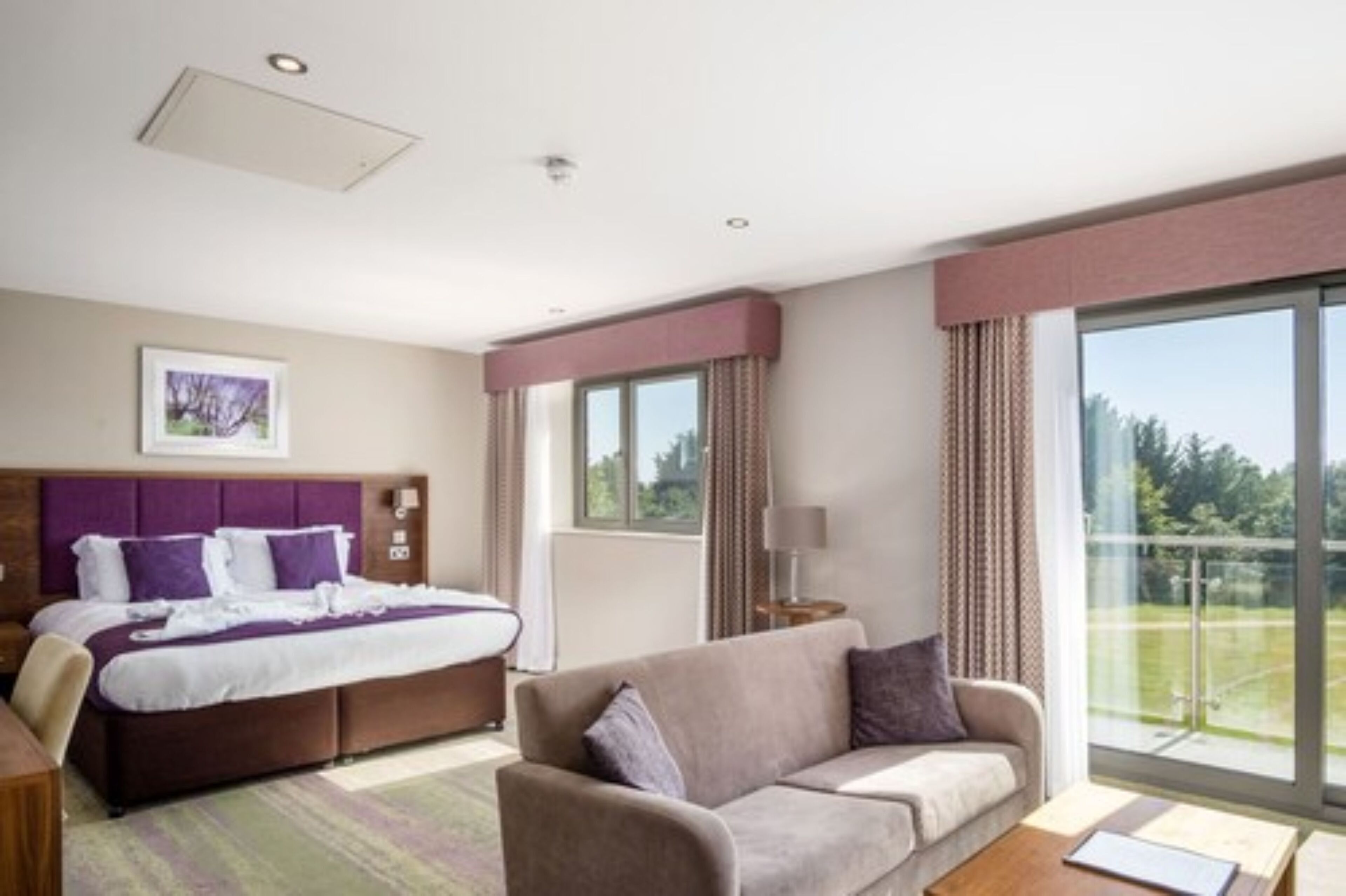 Habitación de hotel con una cama grande, un sofá, un escritorio y un balcón con vistas.
