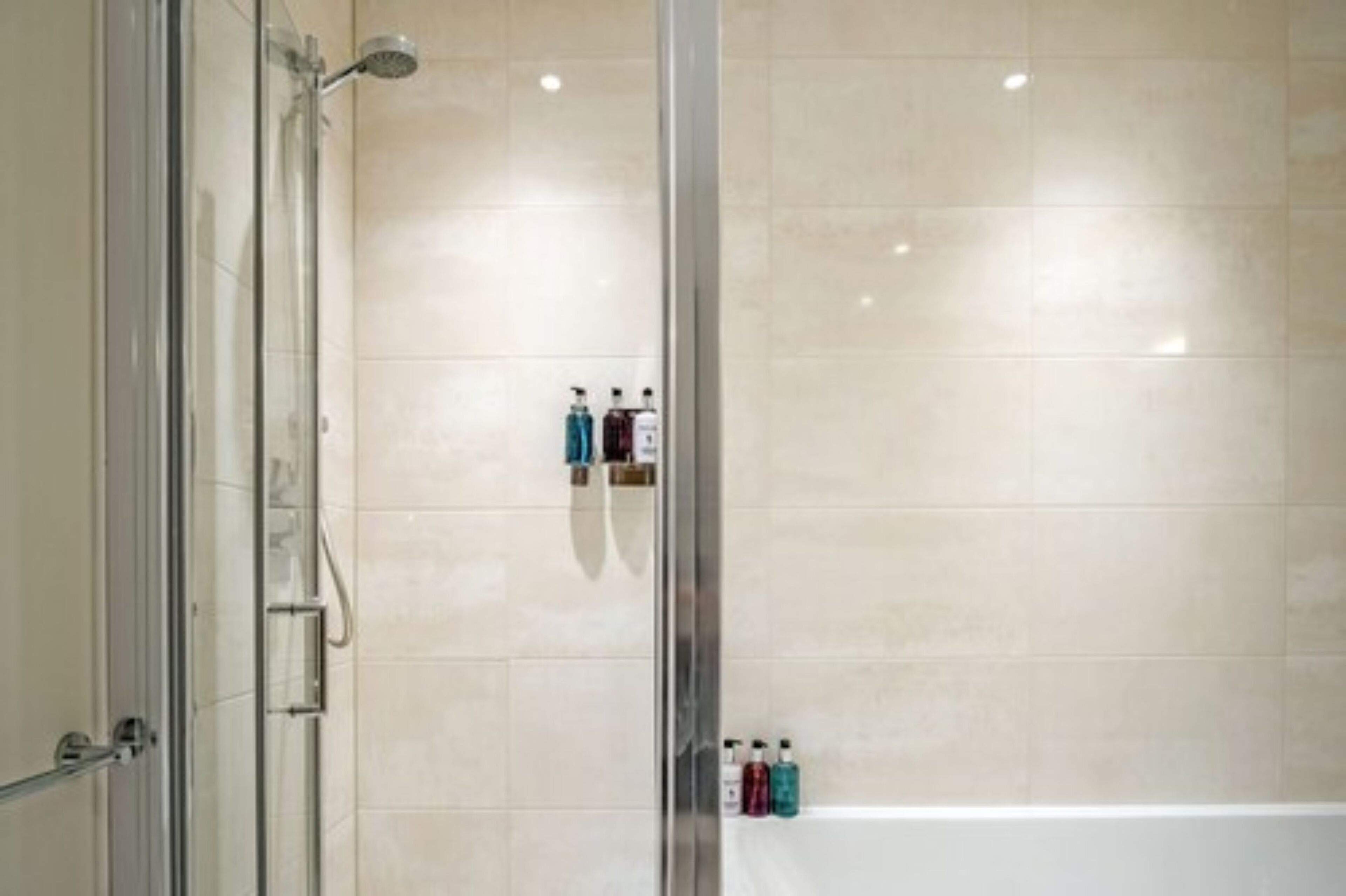 A modern bathroom with a glass shower enclosure, a bathtub, and toiletries on the wall.