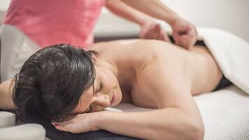A person receiving a massage on a massage table in a room with a white wall and a window.