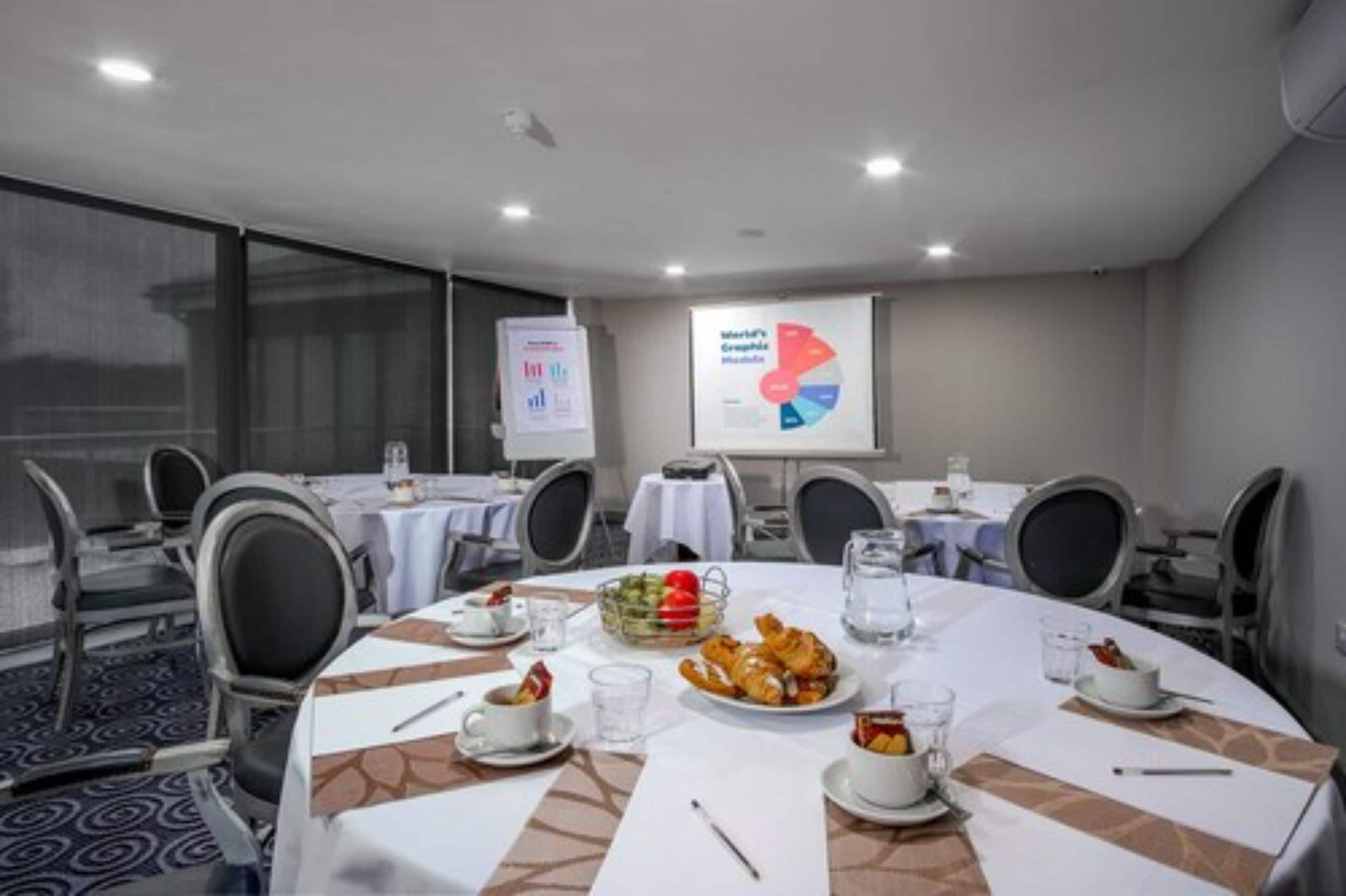 Una sala conferenze con tavoli rotondi, sedie e uno schermo per presentazioni che mostra un grafico a torta.