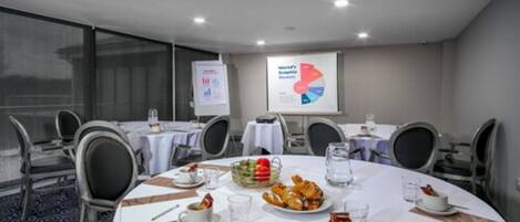 A conference room with round tables, chairs, and a presentation screen displaying a pie chart.