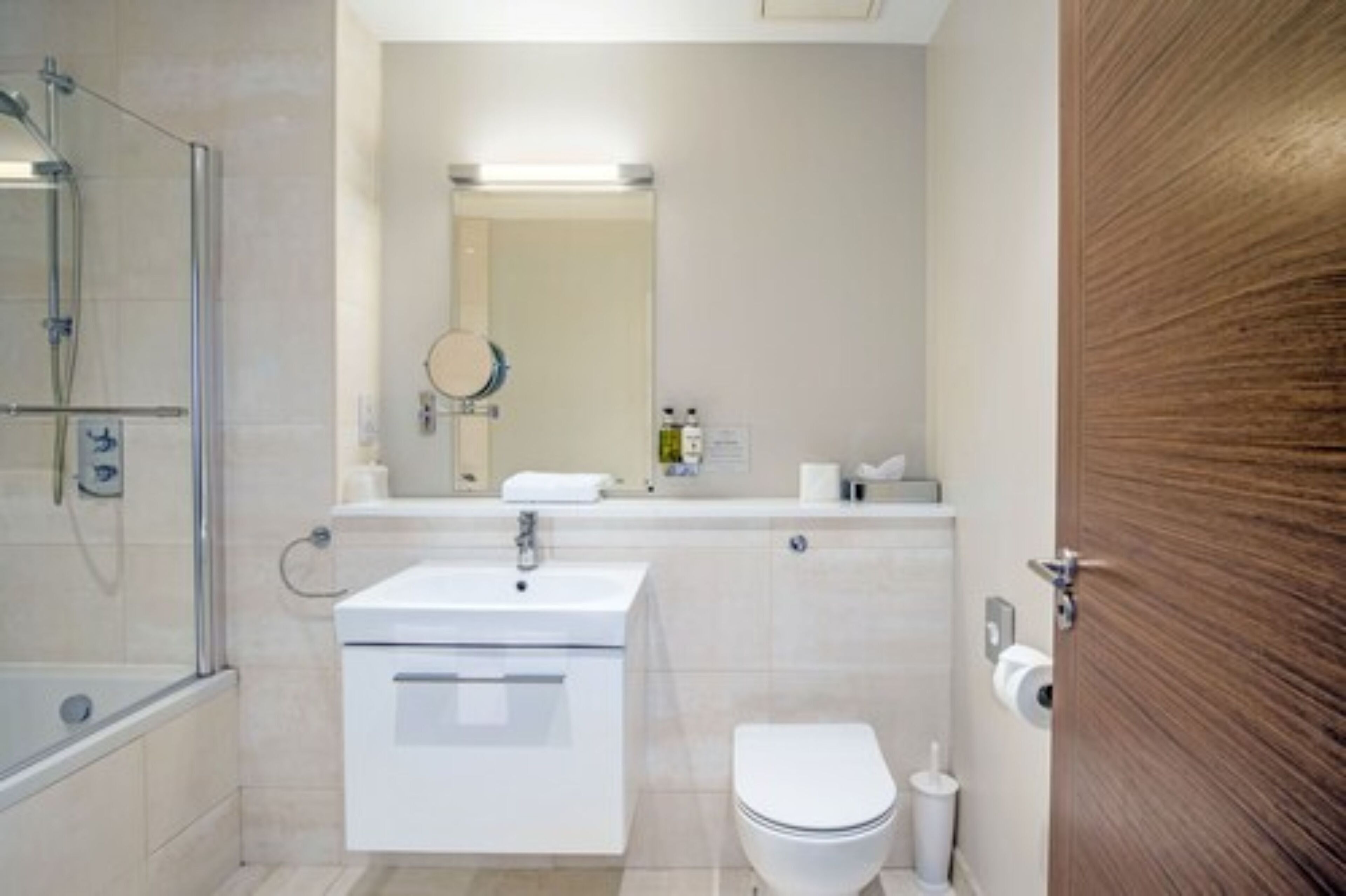 A modern bathroom with a glass shower enclosure, a white sink, a toilet, and a wooden door.