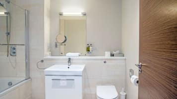 Un baño moderno con cabina de ducha de vidrio, un lavamanos blanco, un inodoro y una puerta de madera.