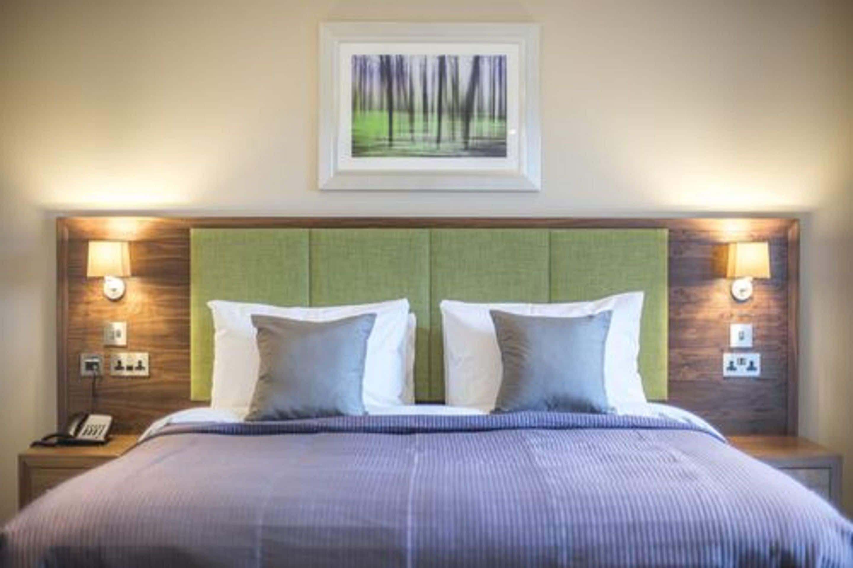 Ein Hotelzimmer mit einem großen Bett, zwei Nachttischlampen, einem gerahmten Bild an der Wand und einem grünen Kopfteil.