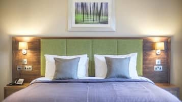 Ein Hotelzimmer mit einem großen Bett, zwei Nachttischlampen, einem gerahmten Bild an der Wand und einem grünen Kopfteil.