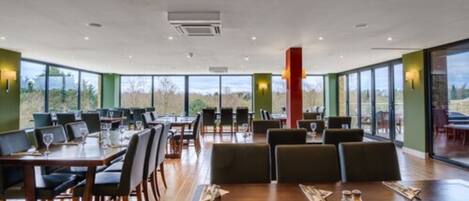 Un comedor amplio con ventanas grandes, mesas de madera y sillas modernas.