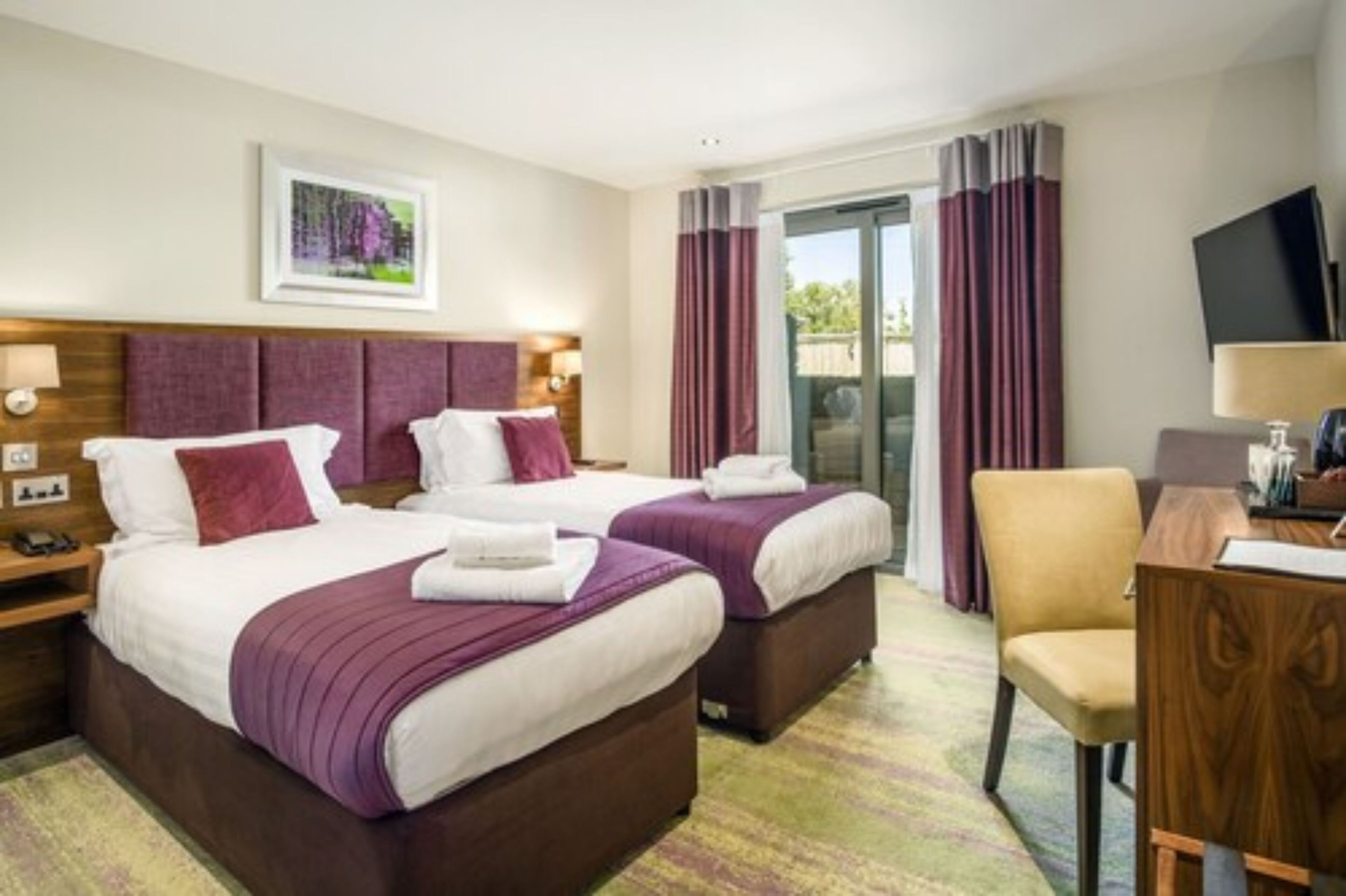 Une chambre d’hôtel avec deux lits, un bureau, une chaise, une télévision et une fenêtre avec des rideaux.