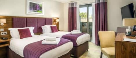 Une chambre d’hôtel avec deux lits, un bureau, une chaise, une télévision et une fenêtre avec des rideaux.