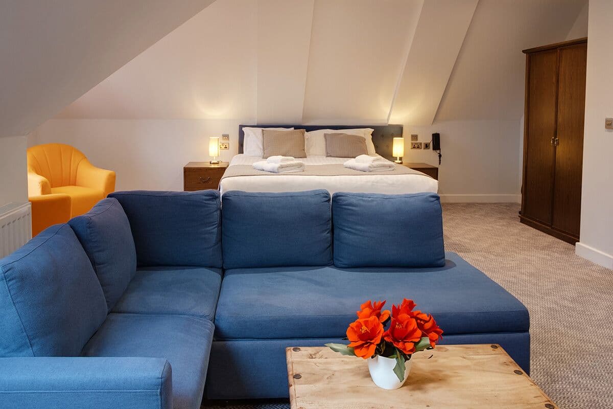 Une chambre moderne avec un grand lit, un canapé bleu et une table basse en bois agrémentée de fleurs.