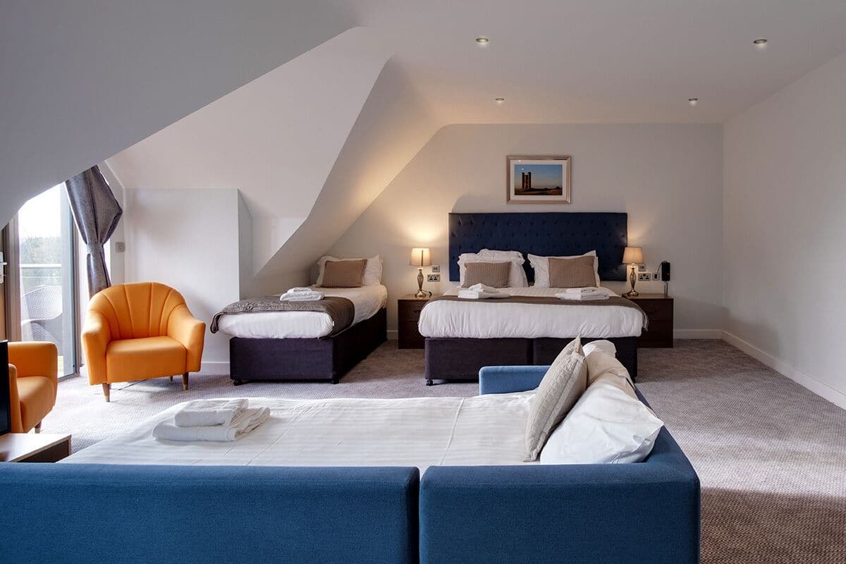 Une chambre d’hôtel moderne avec un grand lit, deux petits lits, un canapé et un fauteuil.