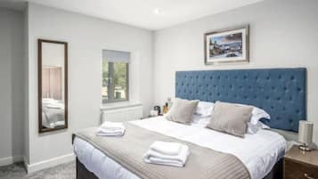 A neatly made bed with a blue headboard, a large mirror, and a framed picture on the wall.
