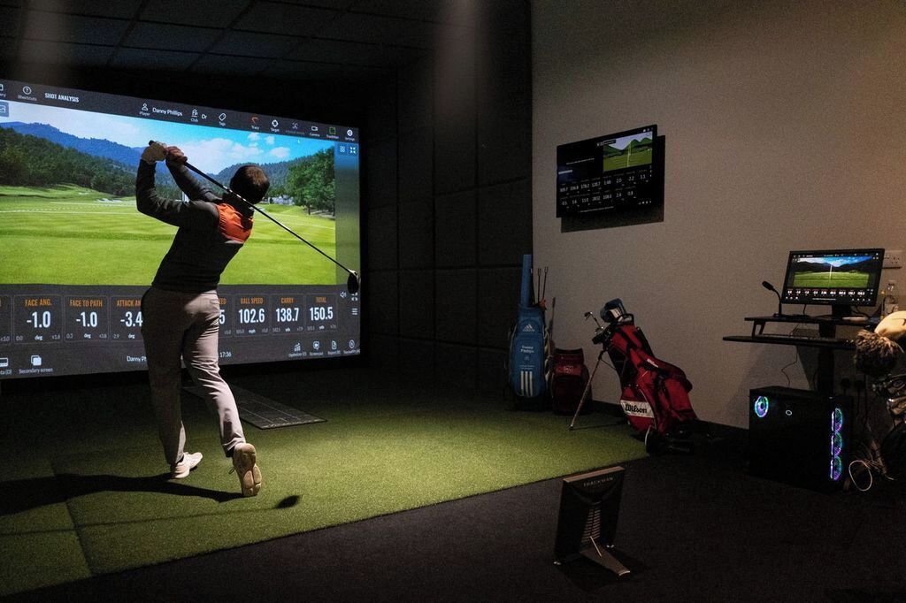 A golfer practicing on a driving range with a large screen displaying a golf simulation.