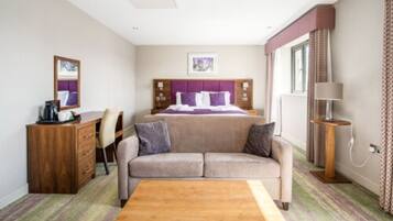 A hotel room with a bed, a sofa, a wooden table, a desk, and a lamp.