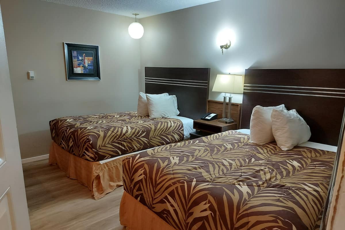 A hotel room with two beds, each with a patterned bedspread, a bedside table with a lamp, and a framed picture on the wall.