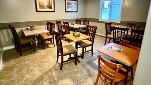 A dining area with stone flooring, wooden tables and chairs, framed pictures on the walls, and a ceiling fan. - Melville Country Inn (Melville)
