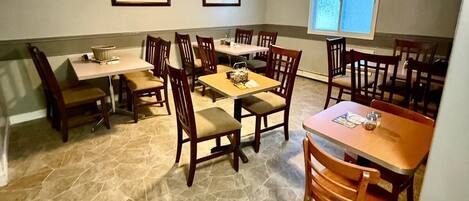 A dining area with stone flooring, wooden tables and chairs, framed pictures on the walls, and a ceiling fan.
