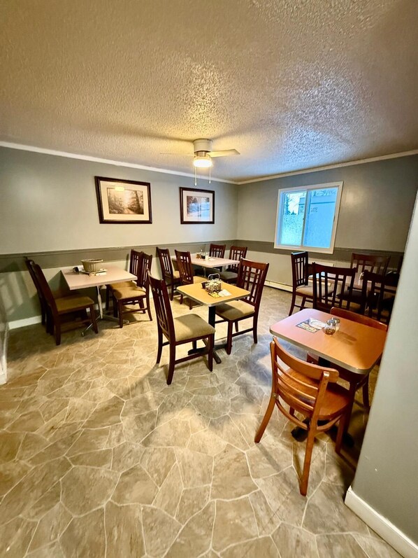 A dining area with stone flooring, wooden tables and chairs, framed pictures on the walls, and a ceiling fan. - Melville Country Inn (Melville)