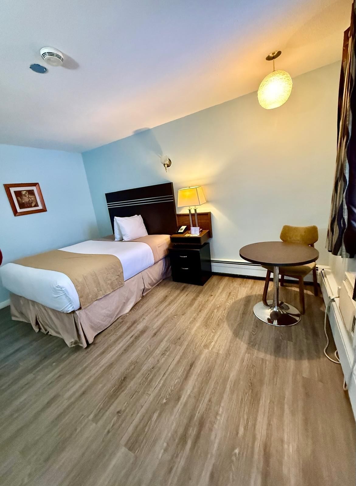 A hotel room with a bed, bedside table, lamp, and a small round table.