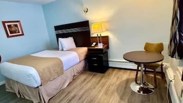 A hotel room with a bed, bedside table, lamp, and a small round table.
