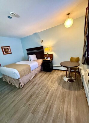 A hotel room with a bed, bedside table, lamp, and a small round table. - Melville Country Inn (Melville)