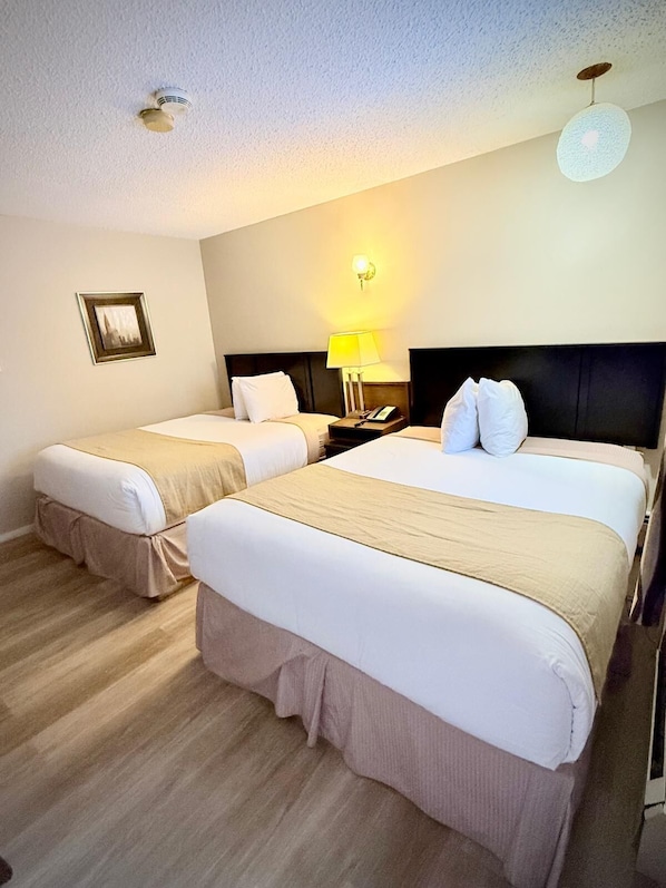 Quarto de hotel com duas camas, uma mesa de cabeceira com abajur, um quadro na parede e um lustre no teto.