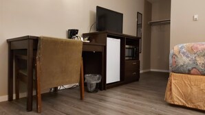 A compact room with a wooden desk, a television, a small refrigerator, and a bed with a patterned cover. - Melville Country Inn (Melville)