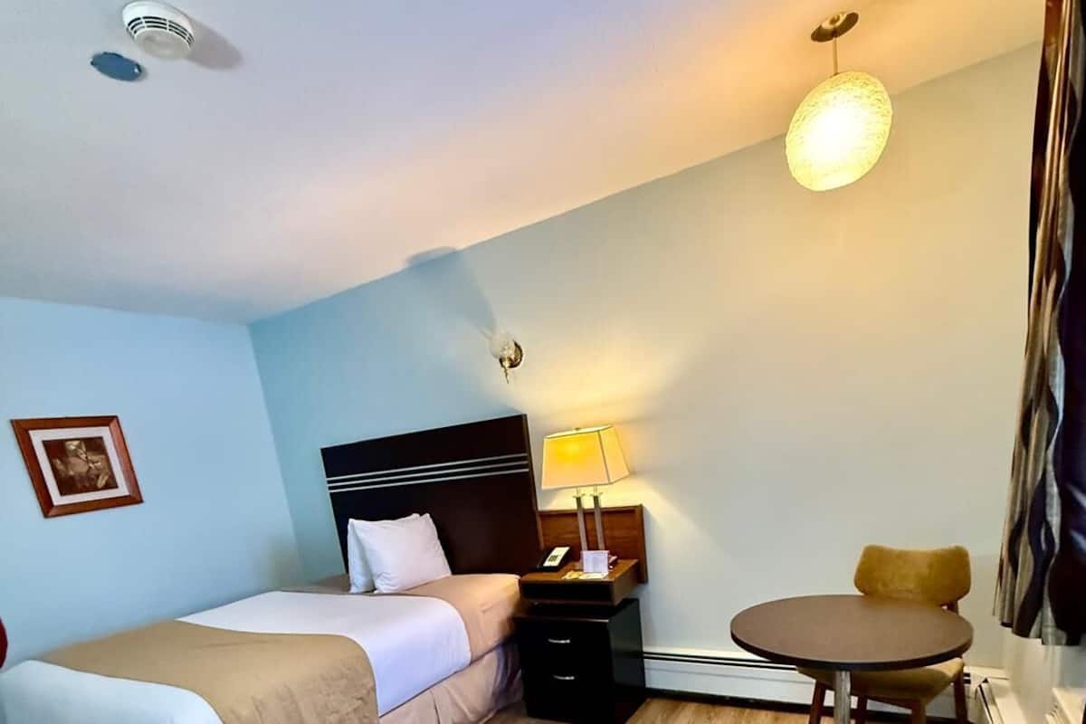 A hotel room with a bed, bedside table, lamp, and a small round table.