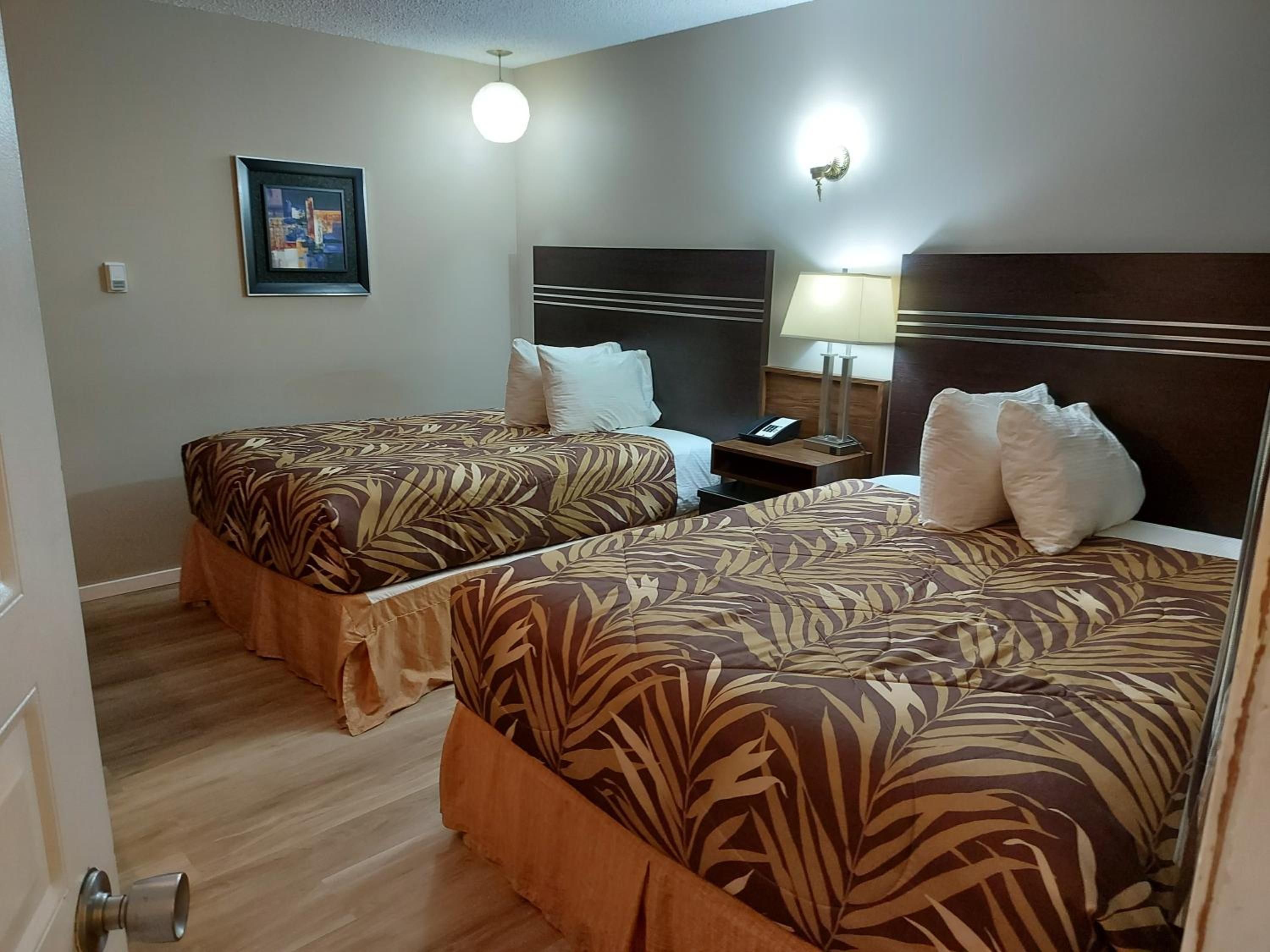 A hotel room with two beds, a bedside table with a lamp, and a framed picture on the wall.