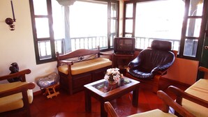 Un salon avec un canapé en bois, un fauteuil en cuir, une table basse en verre et un téléviseur.