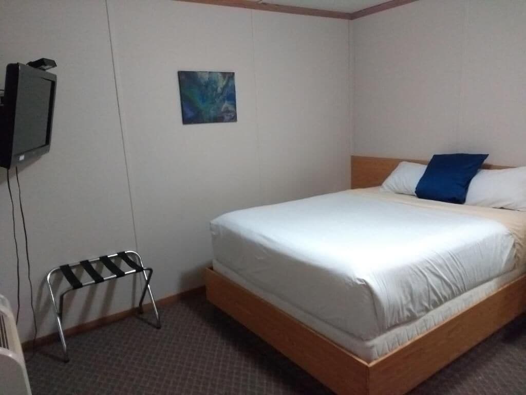 A hotel room with a single bed, a small table, a wall-mounted television, and a painting.