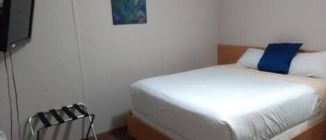 A hotel room with a single bed, a small table, a wall-mounted television, and a painting.