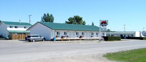 A motel with a green roof, a parking area, and a signboard in the background.