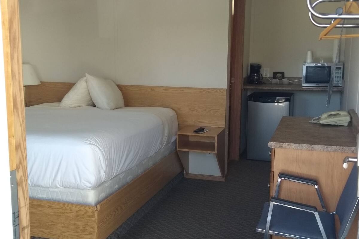 Une chambre d’hôtel comprenant un lit, une table de chevet, un petit bureau avec une chaise, un four à micro-ondes, un téléphone et une machine à café.