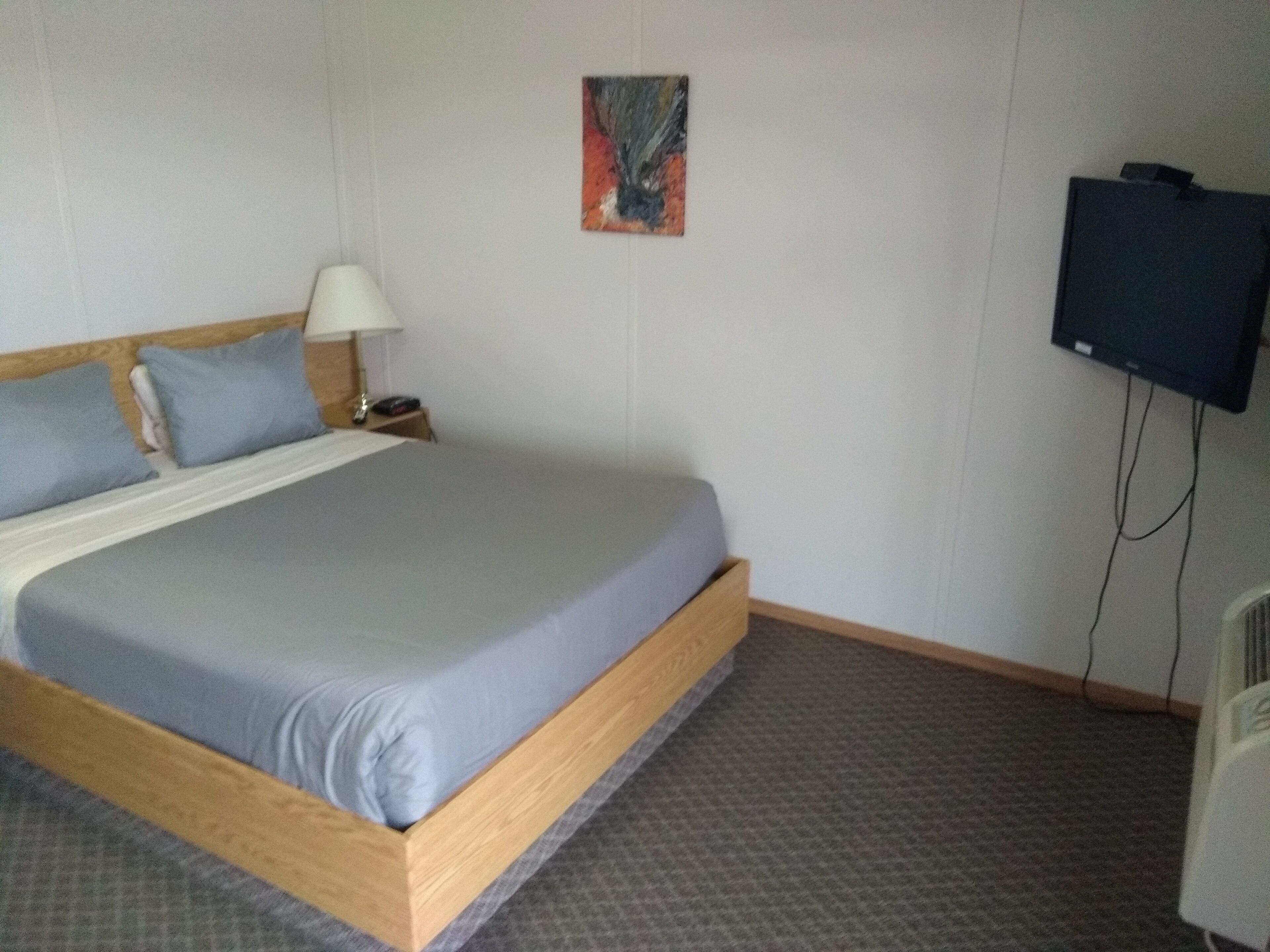 A hotel room with a bed, a nightstand, a lamp, a television, and a painting on the wall.