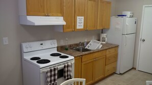 A compact kitchen with wooden cabinets, a white stove, a sink, and a refrigerator. - Sundown Motel (Watrous)