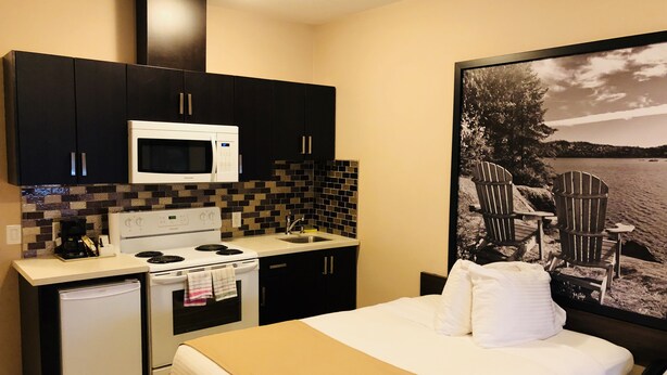 A compact hotel room with a kitchenette, a bed with a beige blanket, and a large poster of a lakeside scene. - Super 8 by Wyndham Watrous (Watrous)