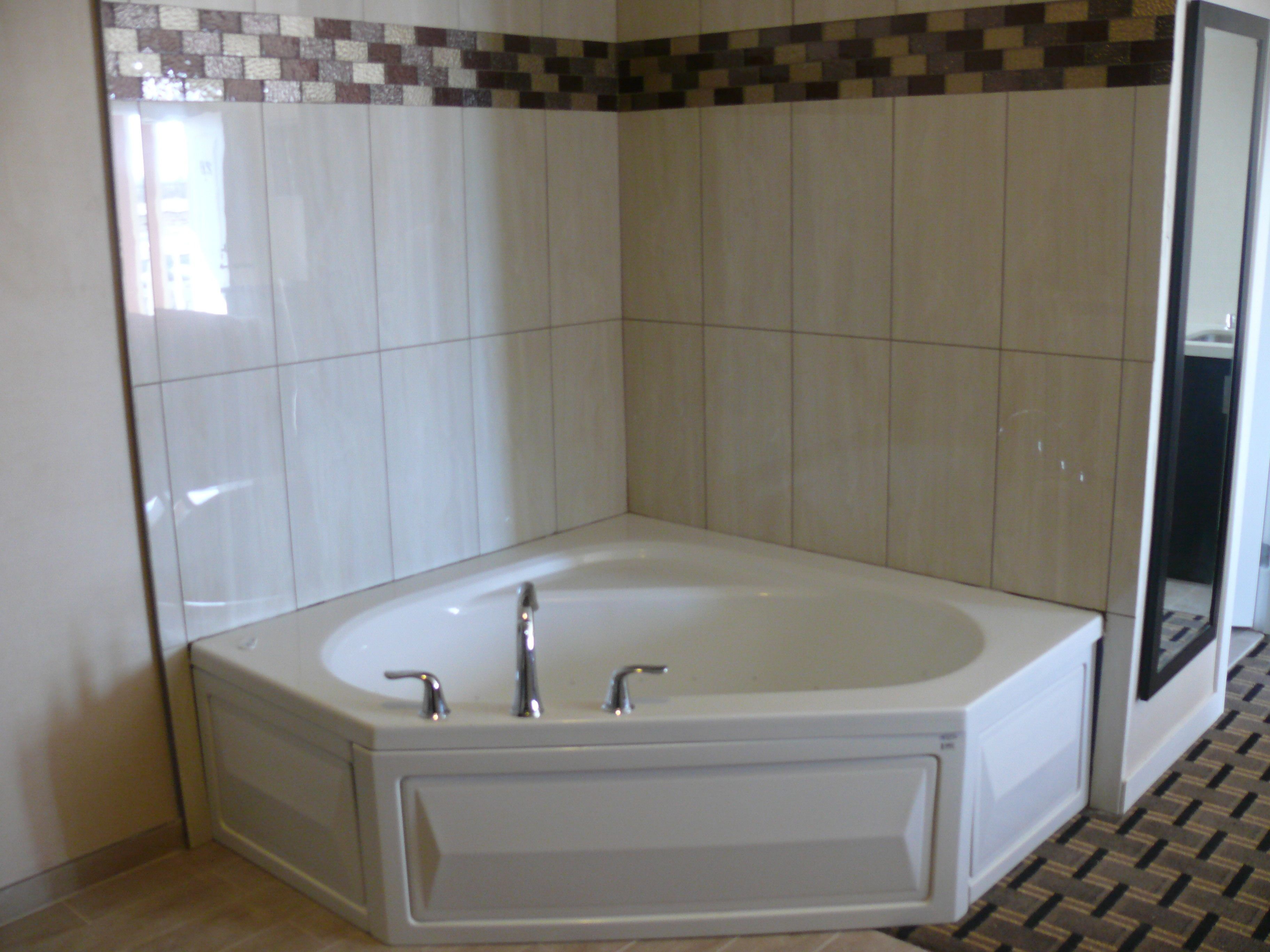 A bathroom with a large bathtub, white tiled walls, and a patterned floor.