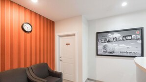 A reception area with a wooden wall, a clock, a framed welcome sign, and a sofa. - Super 8 by Wyndham Watrous (Watrous)