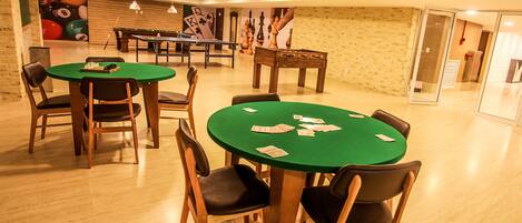 A room with multiple green-topped tables and chairs, a pool table, and a chessboard.