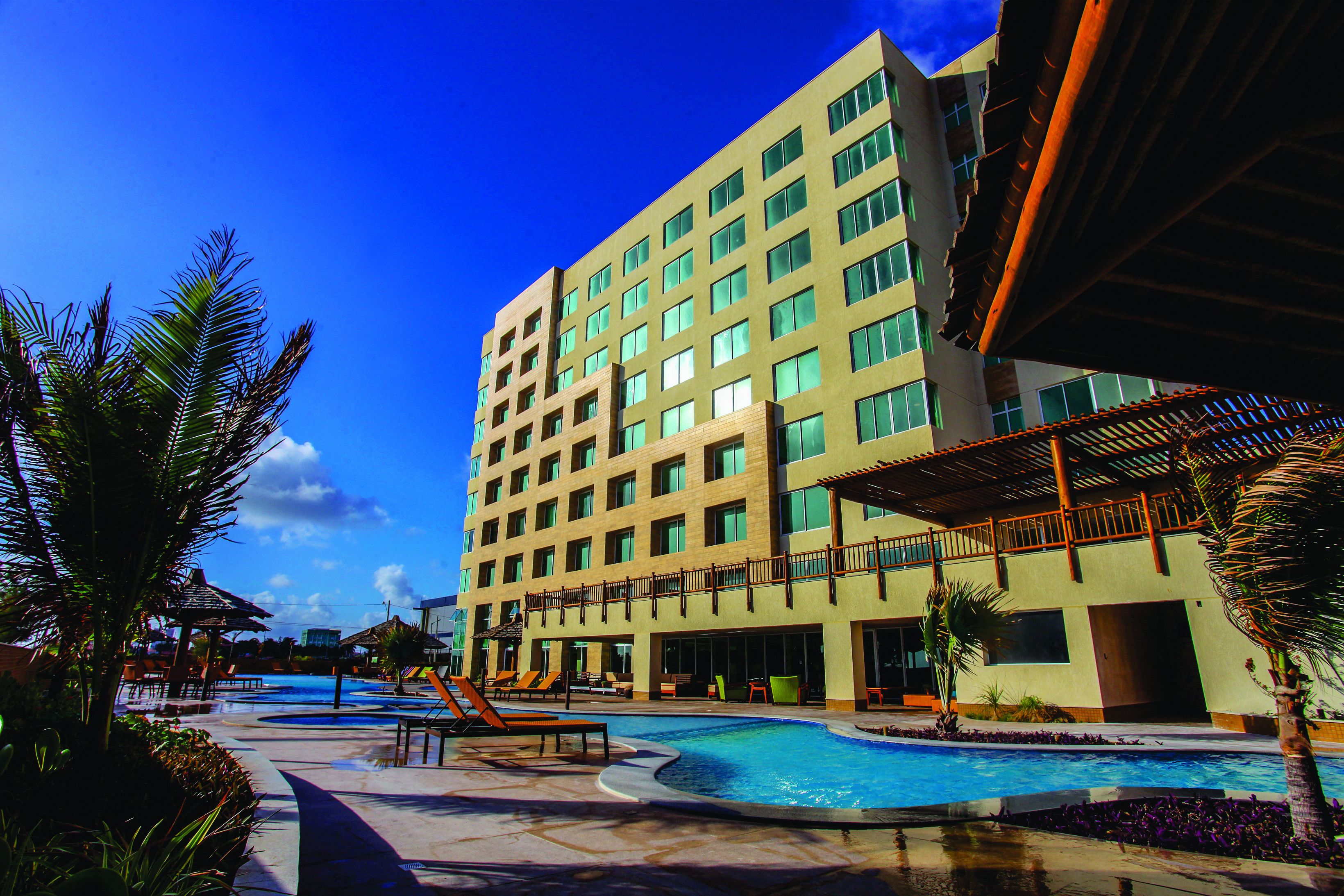 A hotel with a swimming pool, outdoor seating, and a large building with multiple floors.