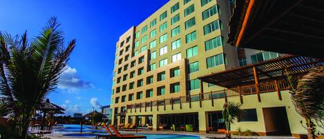 Un hotel con piscina, mobiliario exterior y un edificio grande de varios pisos.