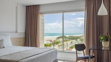 Quarto de hotel com uma janela grande que oferece vista para a praia e o oceano.