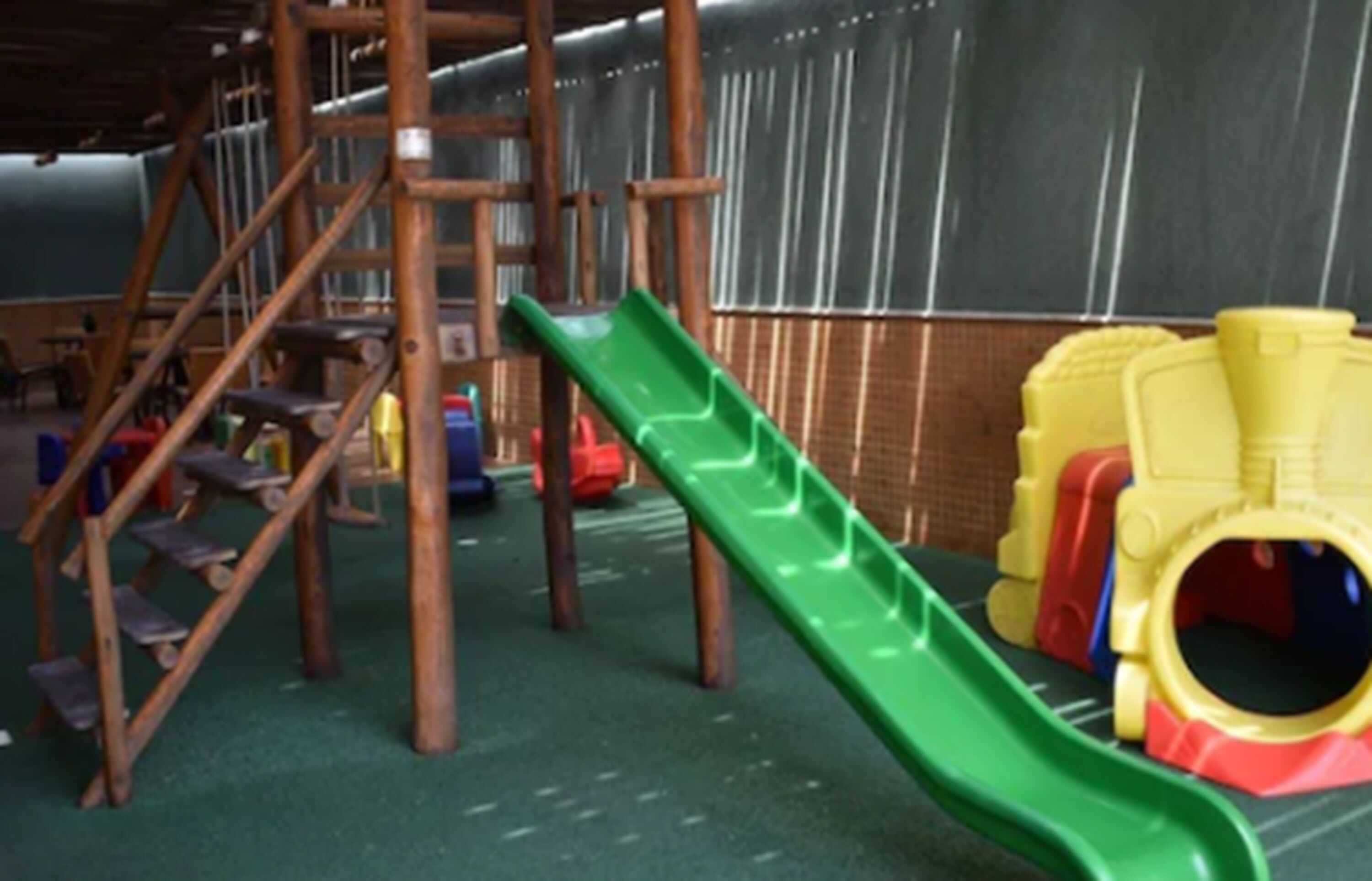 A children's play area with a green slide, wooden climbing structures, and colorful plastic toys.
