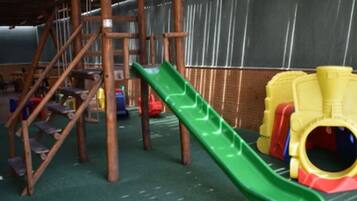A children's play area with a green slide, wooden climbing structures, and colorful plastic toys.