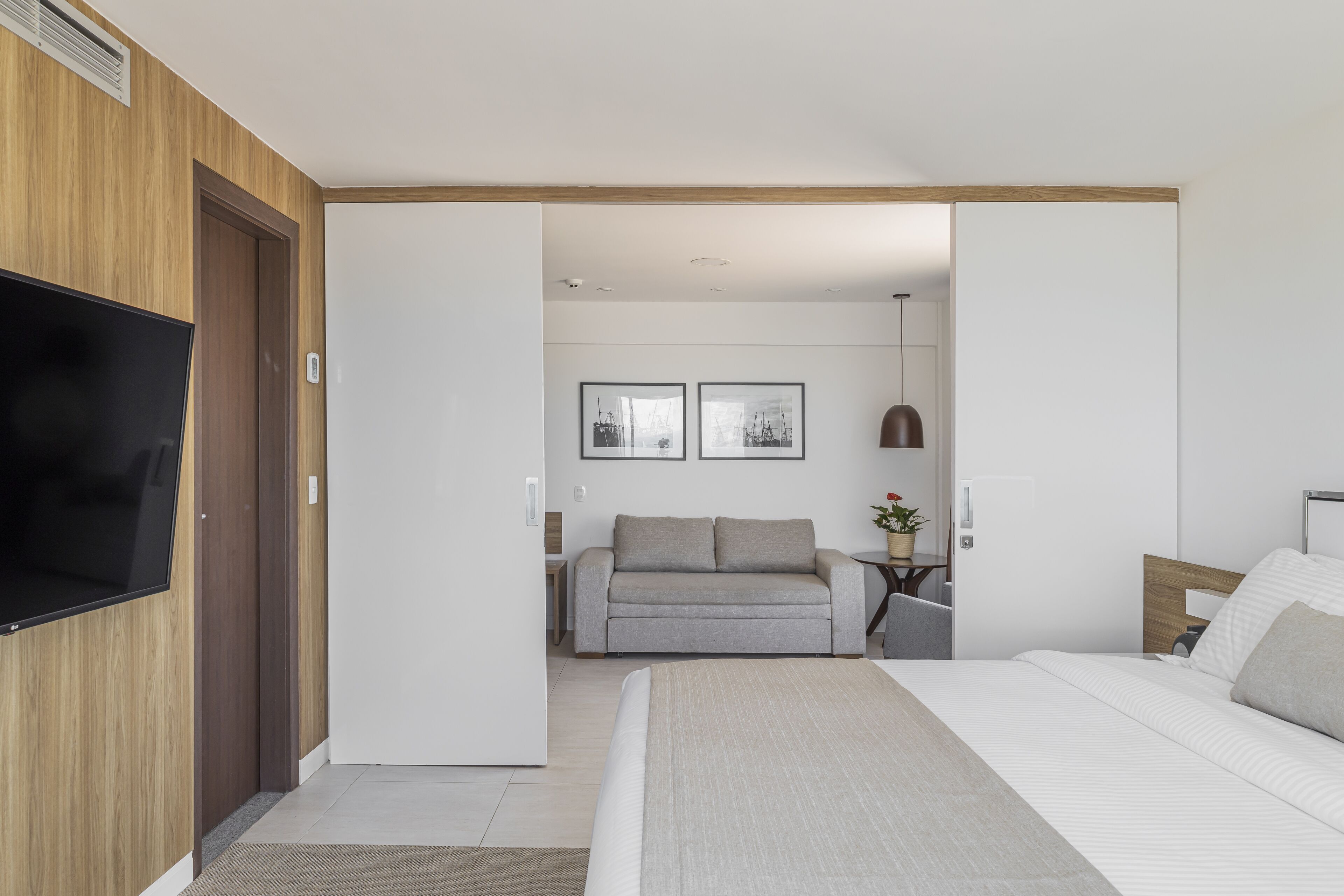 A modern hotel room with a large bed, a flat-screen TV mounted on the wall, a sofa, and two framed pictures on the wall.