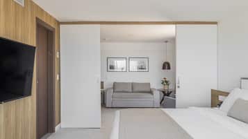 A modern hotel room with a large bed, a flat-screen TV mounted on the wall, a sofa, and two framed pictures on the wall.