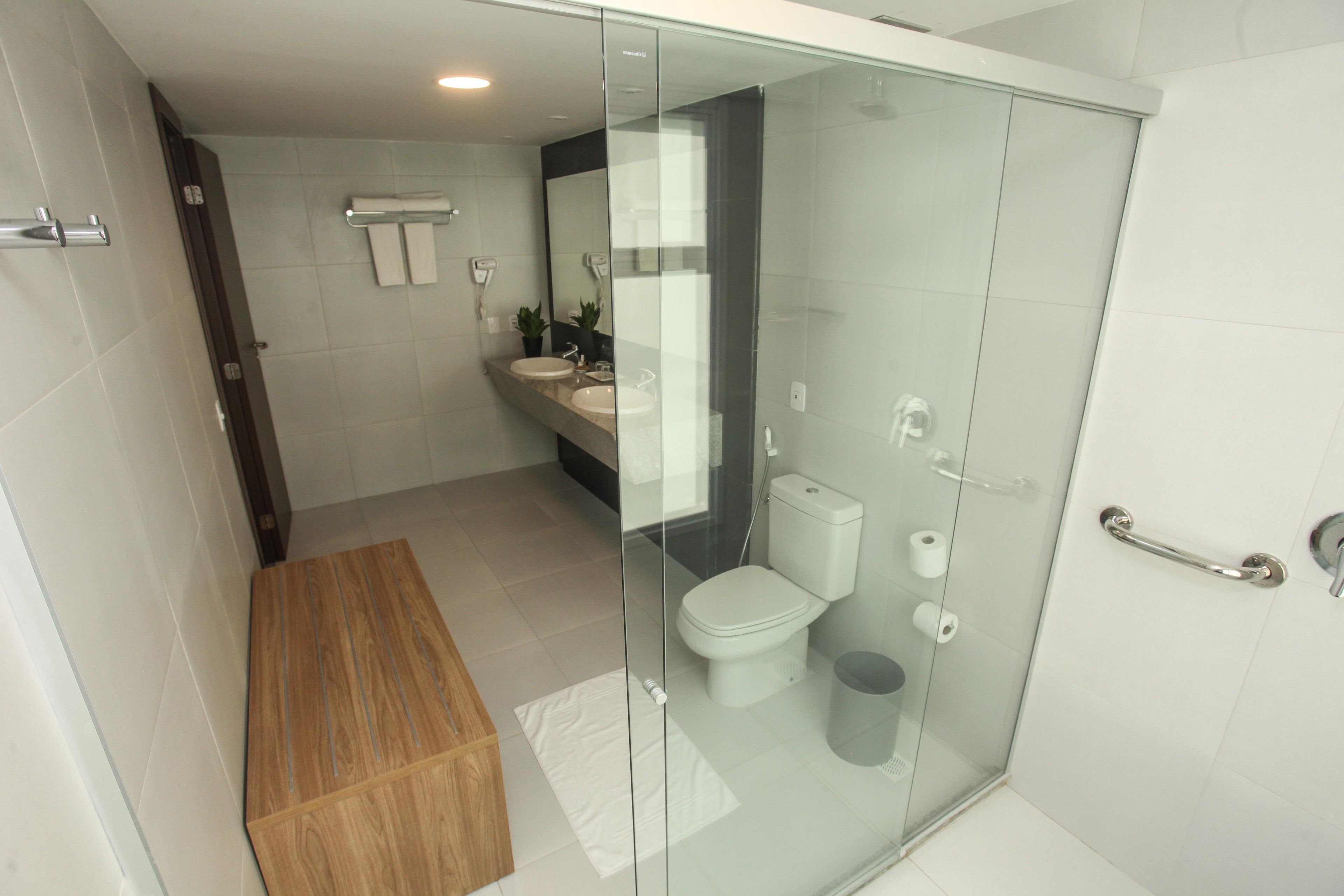 Une salle de bain moderne avec une douche à parois de verre, un banc en bois, un lavabo et des toilettes.