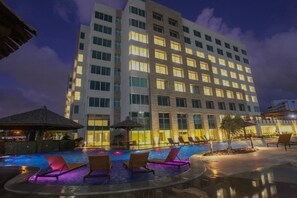 Un hotel con piscina, sillones de descanso y una fachada iluminada.