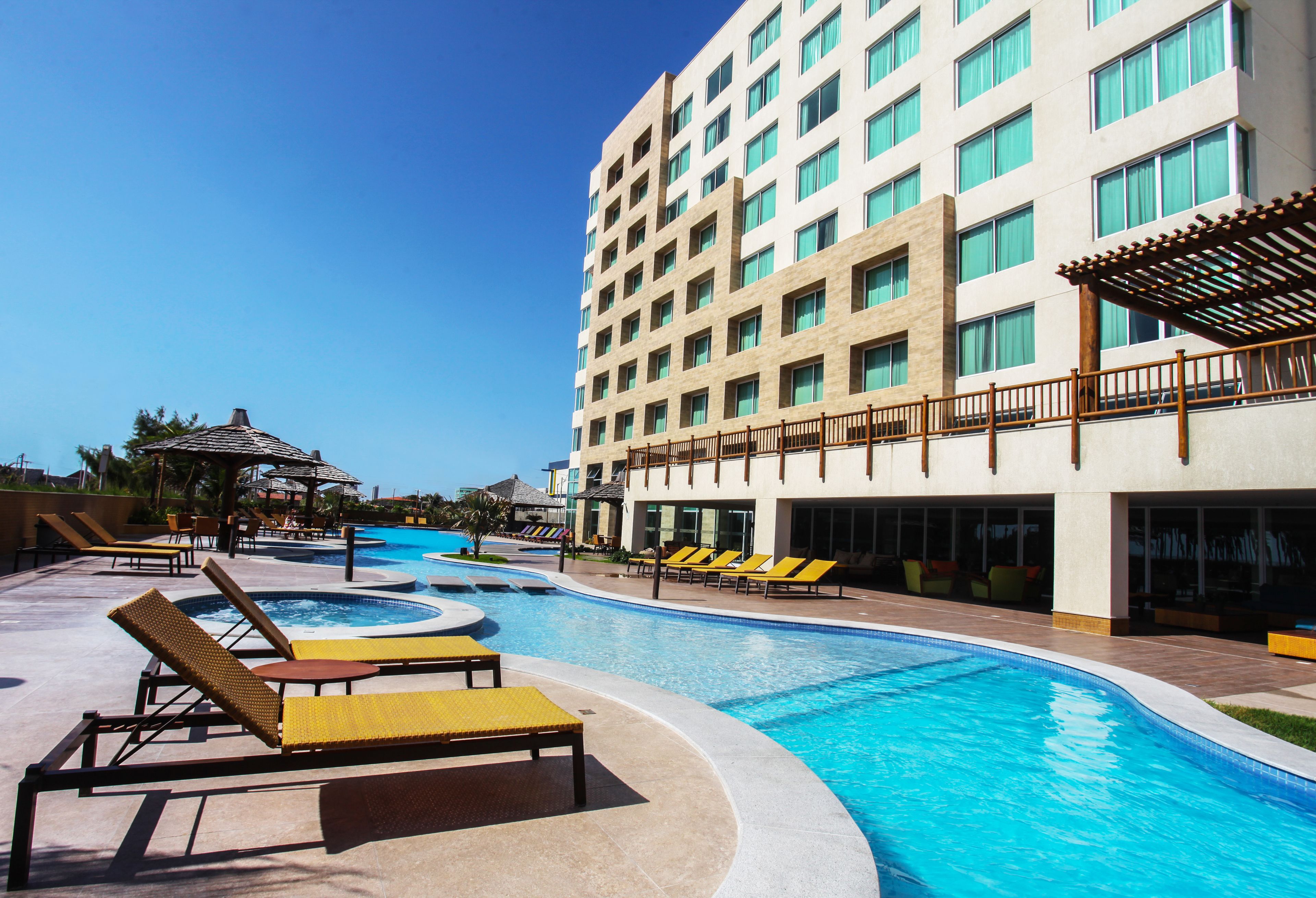 A hotel with a swimming pool, sun loungers, and a covered area.