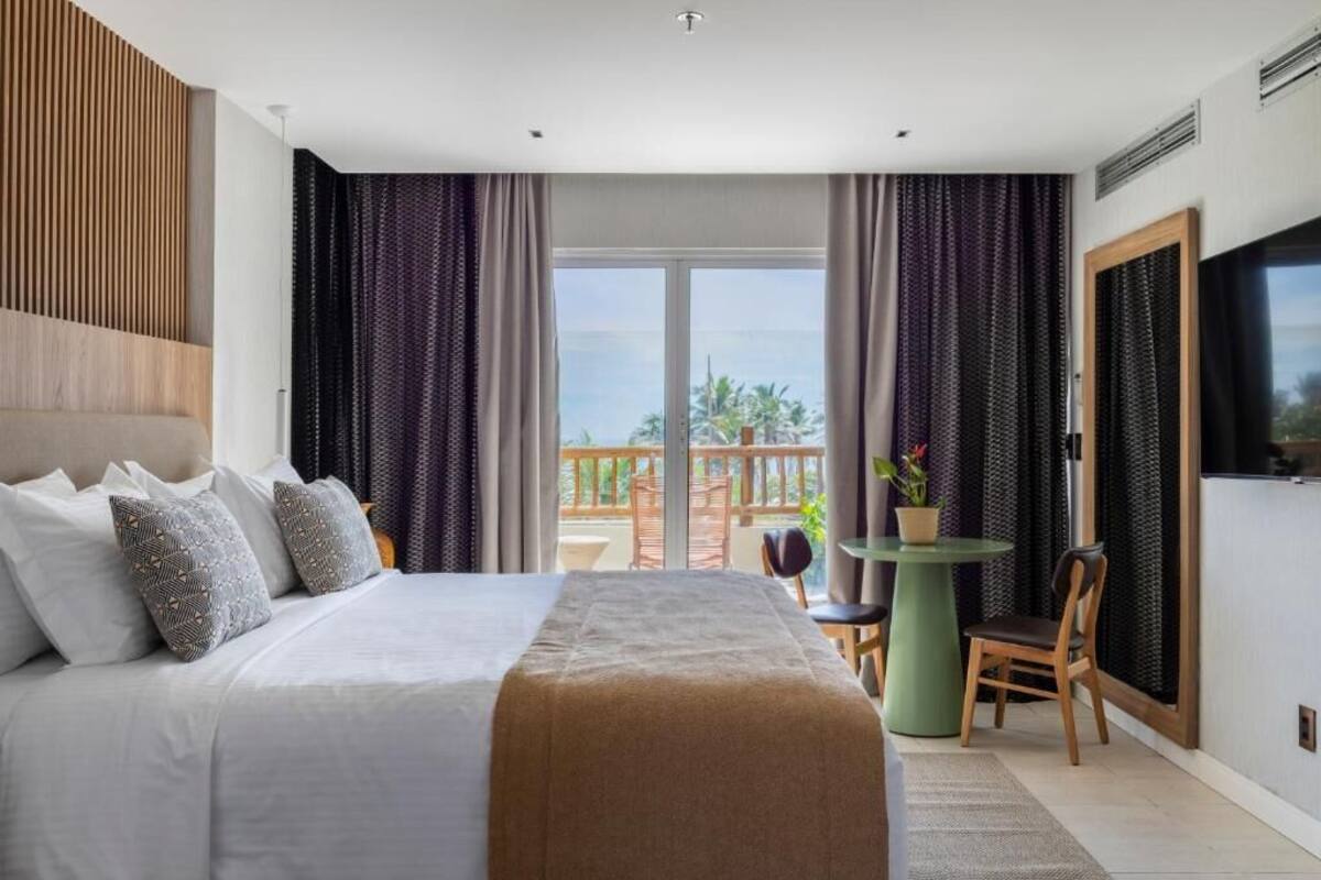 A hotel room with a large bed, a balcony with a table and chairs, and a TV on the wall.